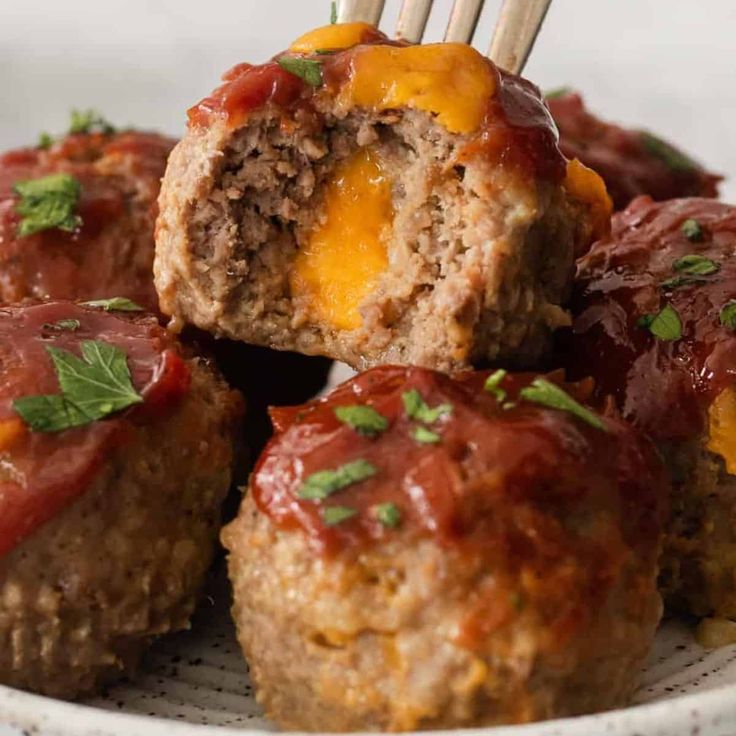 meatballs with ketchup and cheese are on a plate, being held by a fork