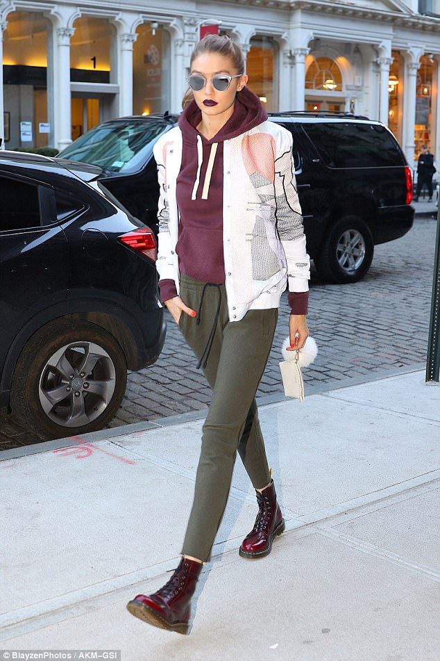 a woman walking down the sidewalk in front of a building wearing sunglasses and a hoodie