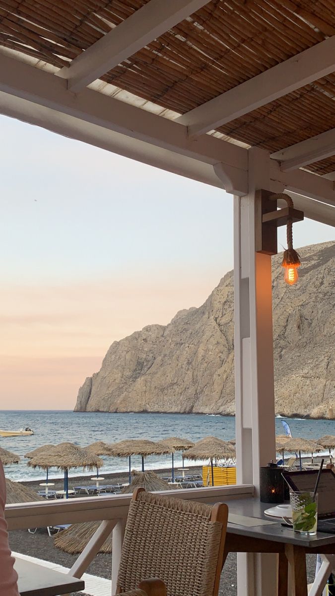 a woman sitting at a table on top of a patio next to the ocean with an open laptop computer