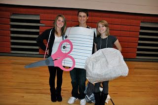 three people standing in a gym holding up a paper cut out with scissors on it