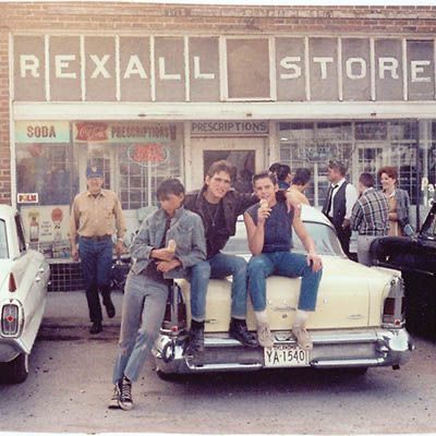 two people sitting on the back of an old car in front of a retail store