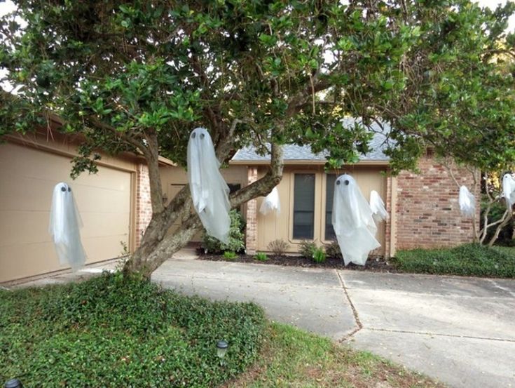 two ghost figures are hanging from a tree in front of a house that is decorated for halloween