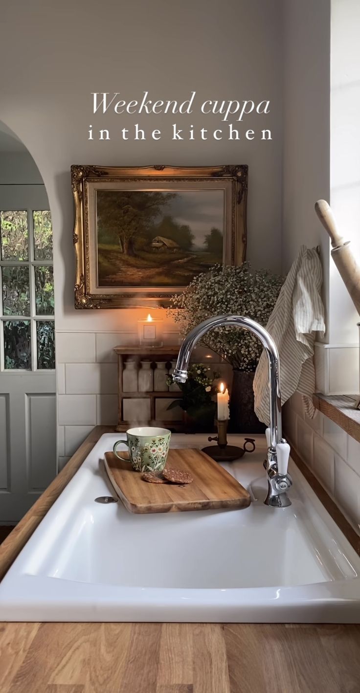 a kitchen sink with a wooden cutting board on top of it next to a painting