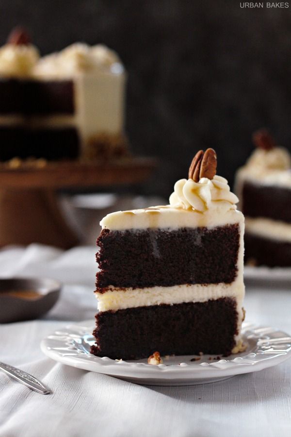 a slice of chocolate cake with white frosting and pecans in the middle on a plate