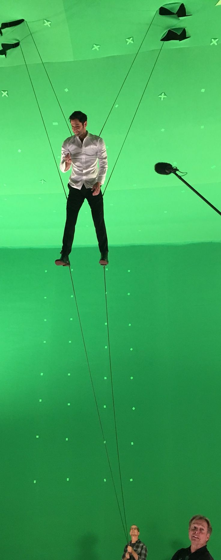 a man is suspended by two strings in front of a green screen with other people