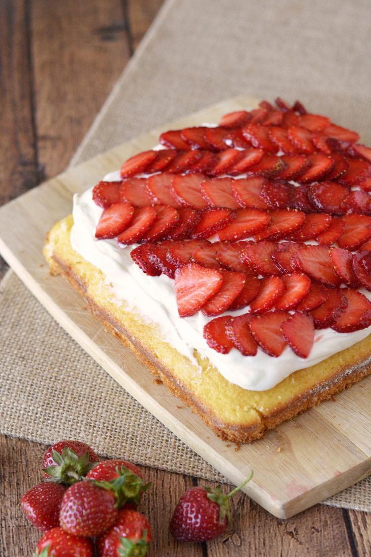 a cake with white frosting and strawberries on it sitting on a cutting board