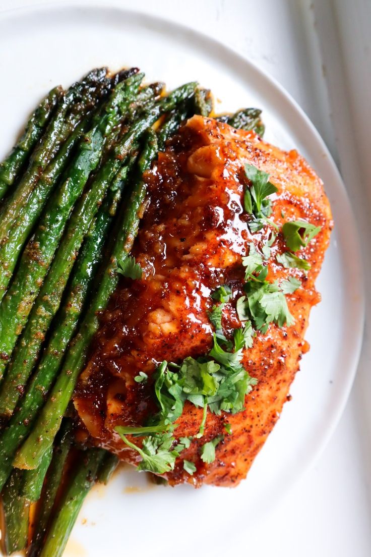 a white plate topped with meat covered in sauce and asparagus next to a fork