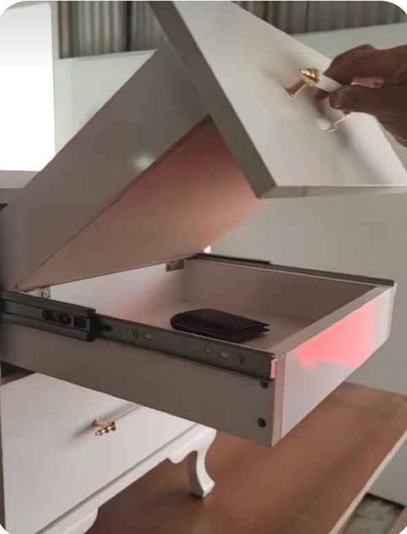 a person opening a drawer on top of a white table with a cell phone in it