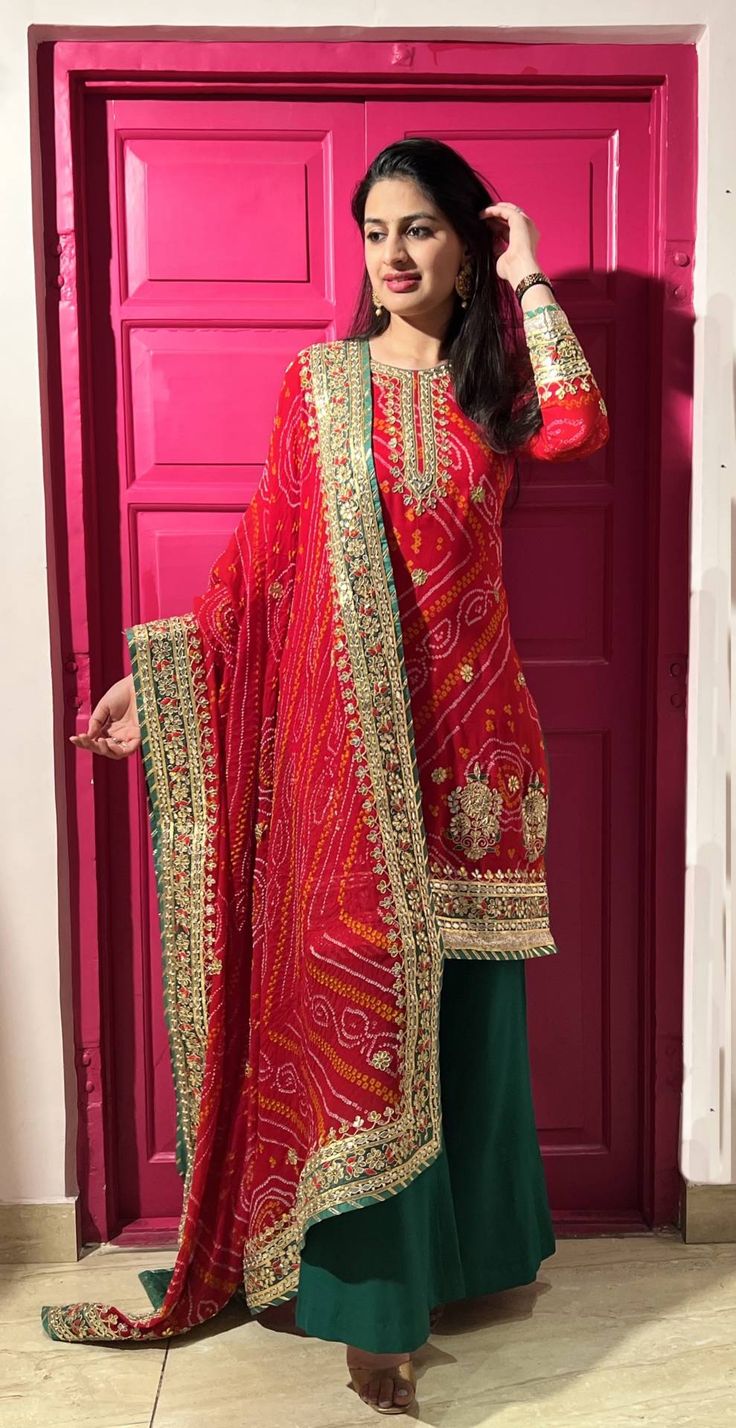 Designer Handmade Red Bandhani Palazzo Set is made in bandhani - hand tie and dye. The beautiful palazzo set has a long neckline with a broad border work on ghera and motifs along with floral buttis. The sleeve also has border design and buttis. The dupatta has beautiful resham and gota work design on all four sides. The suit is teamed with a pure crepe contrast green colored palazzo. The contrast green finishing also brightens up the colour of the suit. Product Highlights Designer Handmade Red