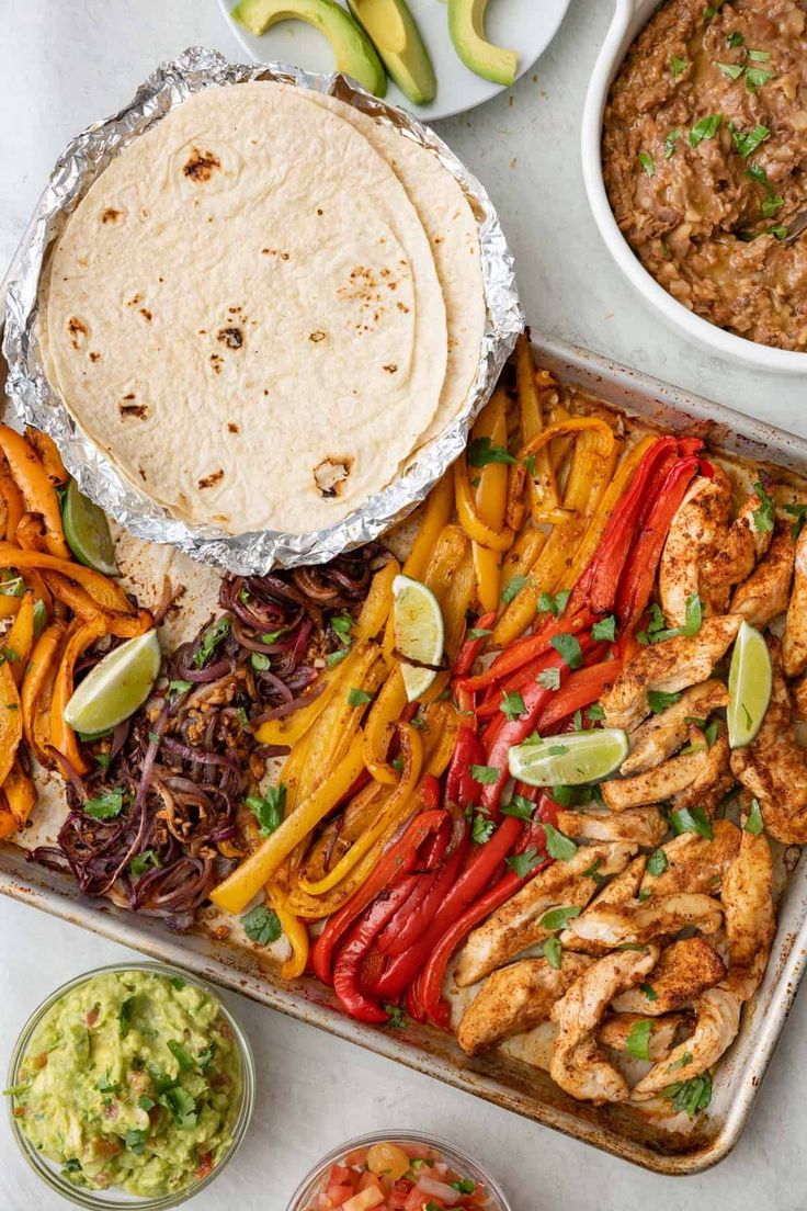 a tray filled with tacos, chicken and other food items next to guacamole