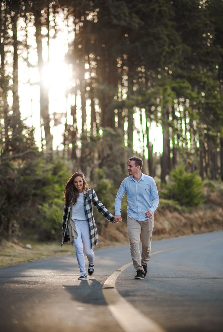 a man and woman walking down the road holding hands with trees in the back ground