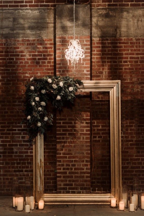 candles are lit in front of an old frame with flowers and greenery on it