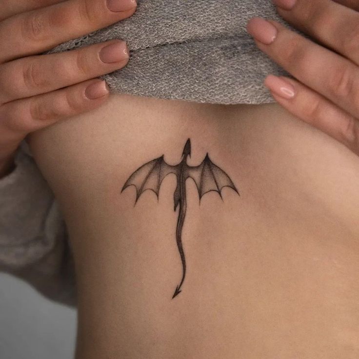 a woman with a bat tattoo on her back and shoulder, behind her are two hands