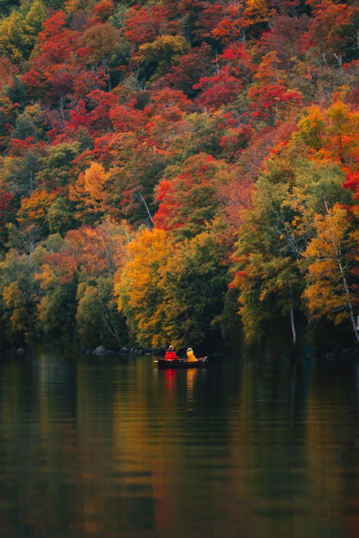 two people in a small boat on a lake surrounded by colorful trees