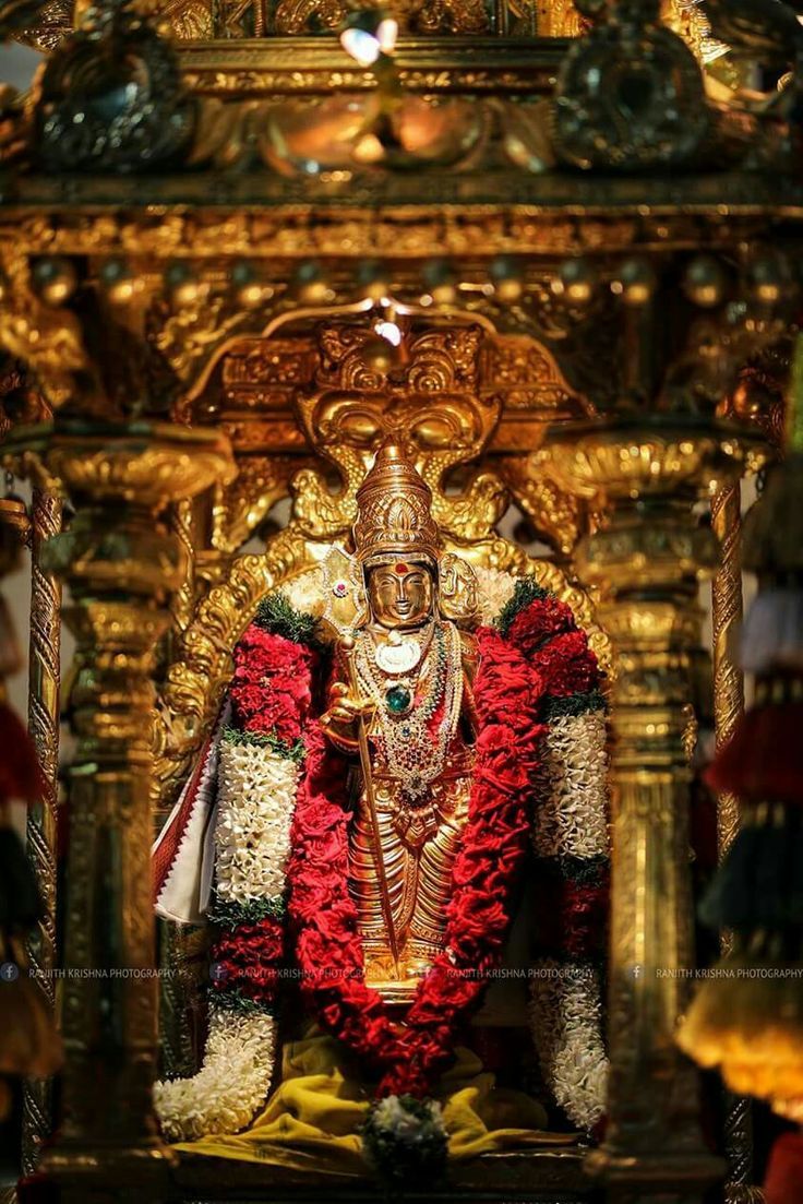 the statue is decorated with red and white flowers in front of an ornate gold alter