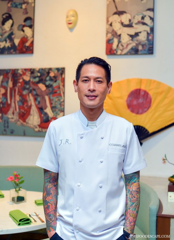 a man in a chef's uniform standing next to some art on the wall