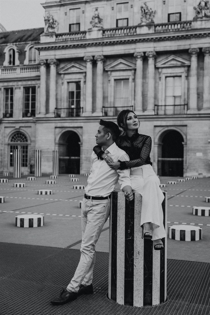 black and white photograph of two people sitting on top of a pole in front of a building