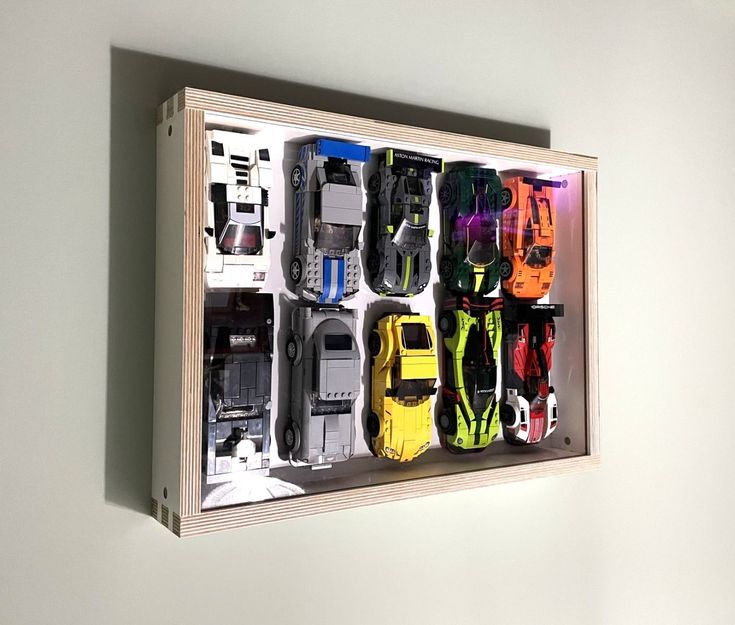 a wooden box filled with lots of different types of toy cars on display next to a wall