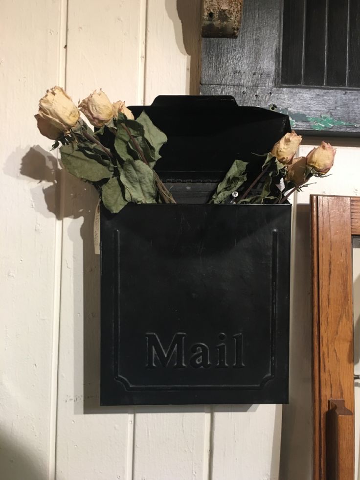 a mailbox with flowers in it hanging on the wall next to a mirror and door