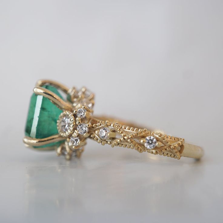 a close up of a ring with an emerald stone and diamonds on the side,