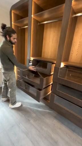 a man standing in front of a wooden cabinet with drawers and shelves on both sides