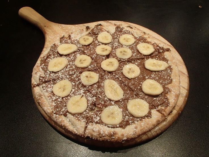 a chocolate pizza with bananas and powdered sugar on the top is ready to be eaten