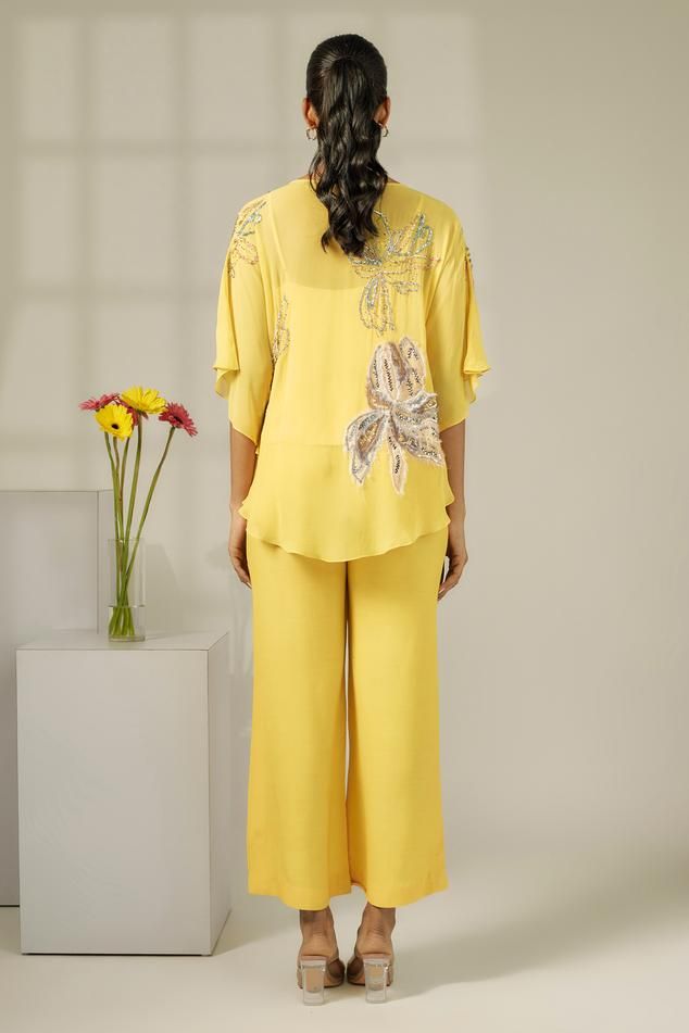 Pastel yellow cape with all over floral patch, sequin and bead embroidery. Paired with bell bottom pants and sleeveless inner slip.
Components: 3
Pattern: Embroidered
Type Of Work: Sequin, Beads and Floral Patch Work
Neckline: Round Neck
Sleeve Type: Cape: Batwing Sleeves, Inner Slip: Sleeveless
Fabric: Cape: Viscose Georgette, Pant: Viscose Crepe, Inner Slip: Viscose Satin
Color: Yellow
Other Details: 
Asymmetric cape hem
Model height: 5ft 6inches, wearing size S
Occasion: Party - Aza Fashions Yellow Embellished Designer Wear Sets, Designer Yellow Embellished Sets, Yellow Embroidered Palazzo Set For Party, Festive Yellow Pant Set For Party, Festive Yellow Party Pant Set, Festive Hand Embellished Yellow Set, Festive Yellow Hand Embellished Set, Spring Silk Sets With Hand Embellished Details, Spring Silk Sets Hand Embellished