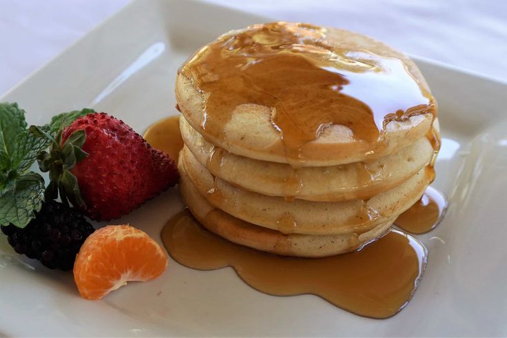 a stack of pancakes on a plate with syrup and fruit