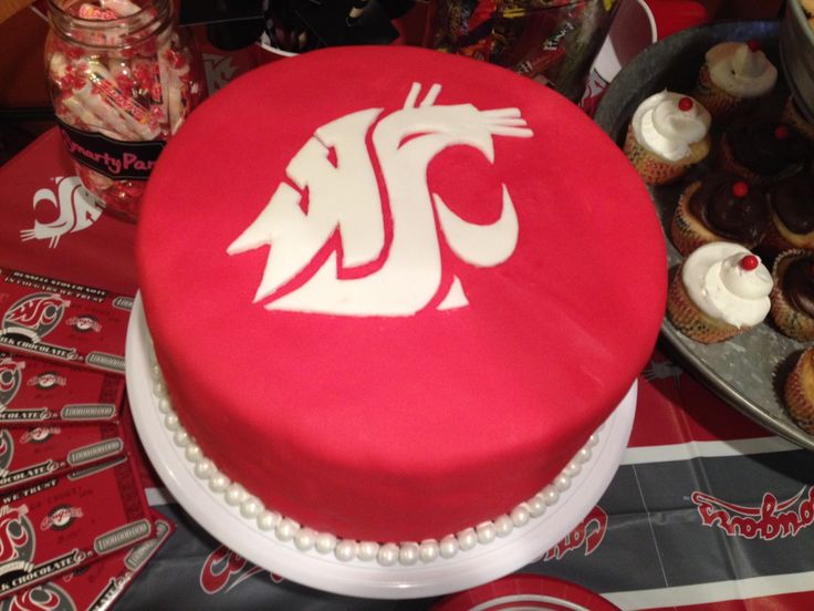 a red cake with white icing sitting on top of a table next to cupcakes