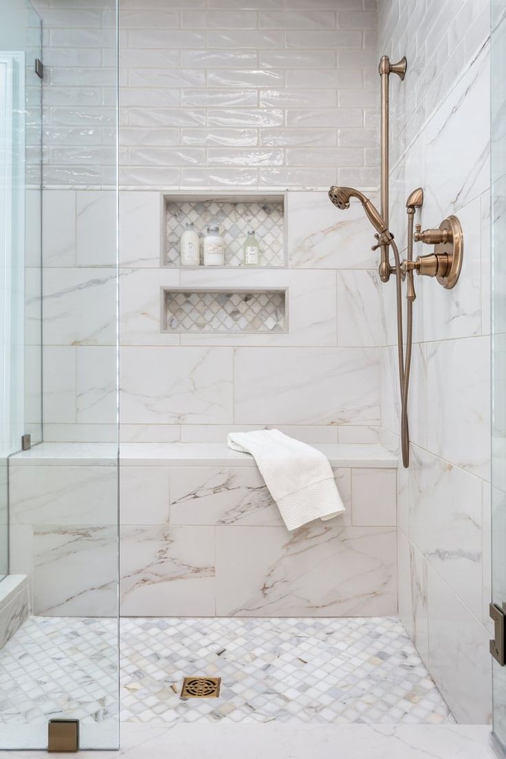 a bathroom with white marble and gold fixtures, including a glass shower door that is open to the bathtub