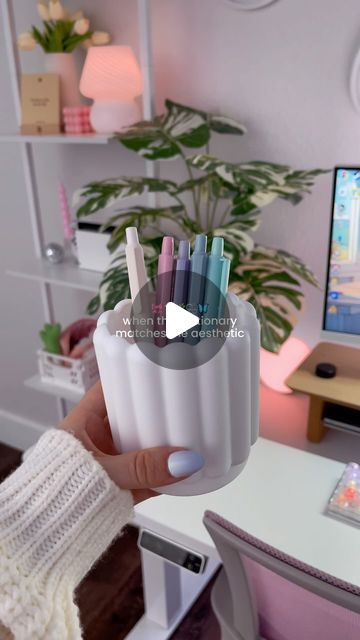 a person holding a cup full of pens in front of a computer desk with a monitor