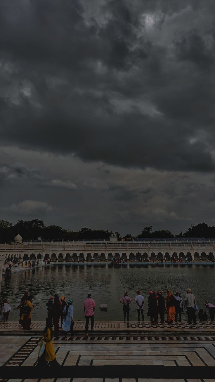 many people are standing in front of a large body of water under a cloudy sky