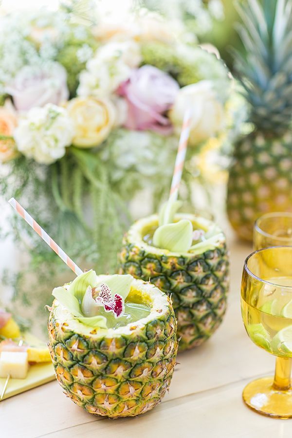 two pineapple drink glasses with straws in them on a table next to flowers