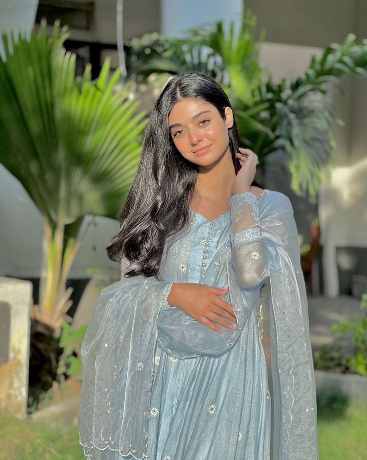 a woman in a blue dress is posing for a photo with her hand on her shoulder