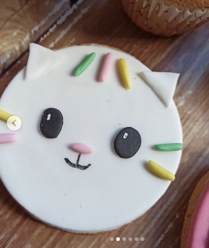 a white cat cake sitting on top of a wooden table next to cupcakes