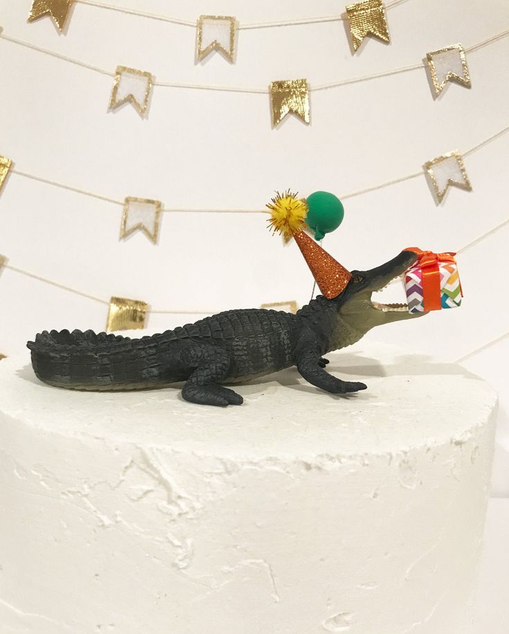 a birthday cake with a toy alligator holding a party hat