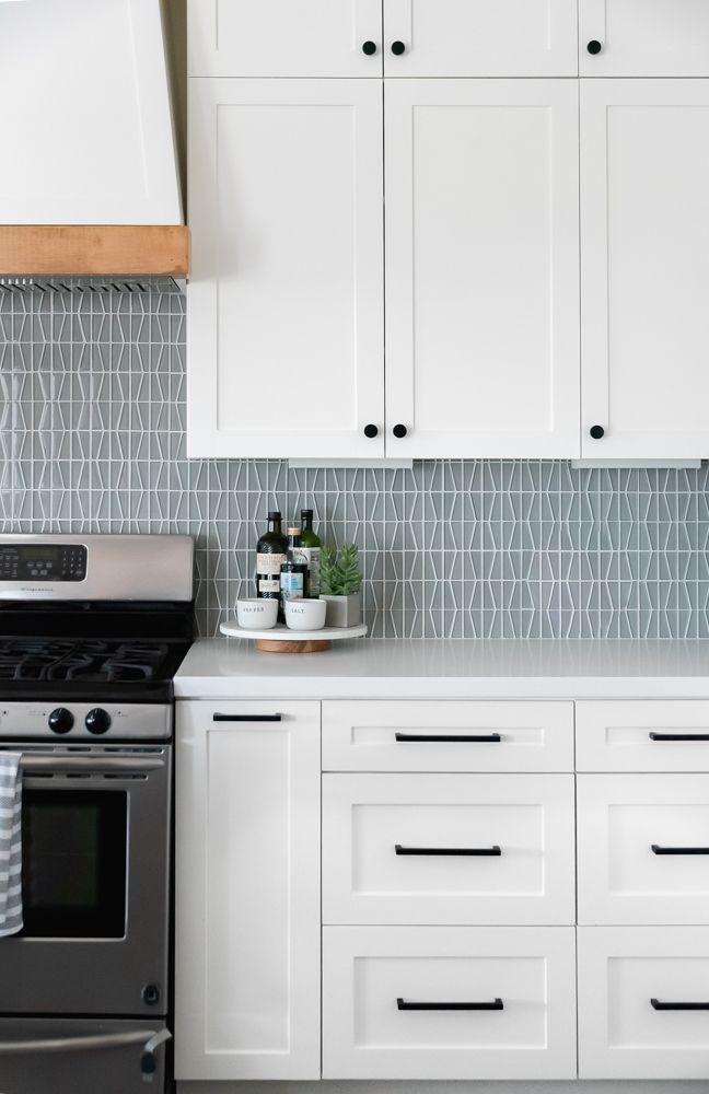 a kitchen with white cabinets and stainless steel stove top oven in front of an oven hood