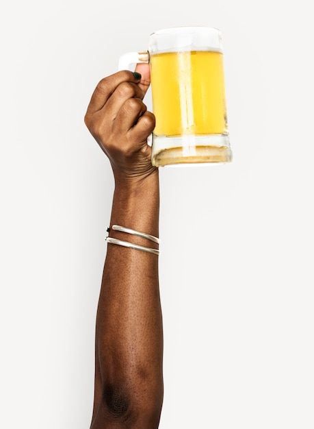 a person holding up a glass of beer in their right hand, with both hands on top of each other