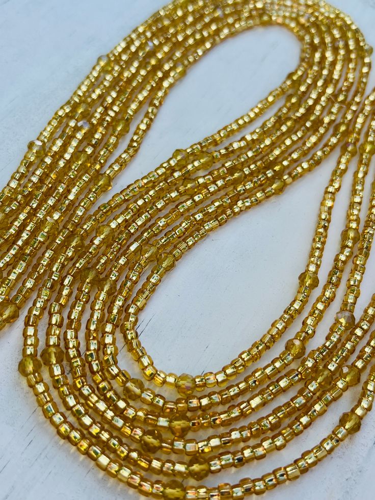 Description One 50 inch tie-on luxury waist bead Created on a durable Ghanian string Shimmery gold seed beads with faceted gold crystals Adjustable Gold Oval Waist Beads, Elegant Multi-strand Gold Beads, Gold Beaded Necklaces With Polished Beads For Party, Gold Multi-strand Jewelry With Polished Beads, Gold Multi-strand Necklace With Gold Beads, Gold Beaded Necklace For Parties, Adjustable Gold Beaded Necklaces With Oval Beads, Gold Beads With Beaded Chain For Party, Adjustable Gold Waist Chain With Colorful Beads