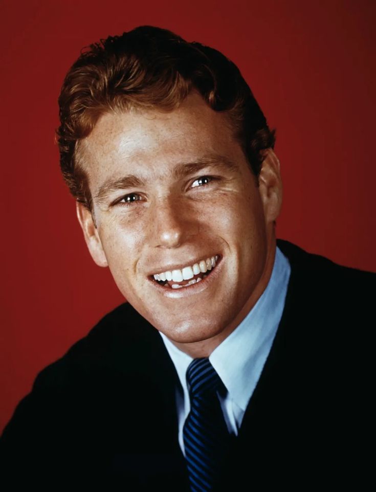 a man in a suit and tie smiling at the camera with a red wall behind him