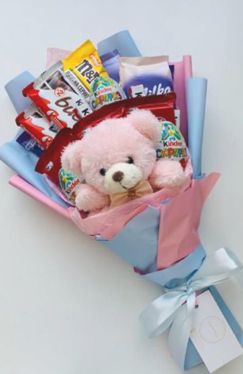 a pink teddy bear sitting in a bouquet of candy and candies with a blue ribbon