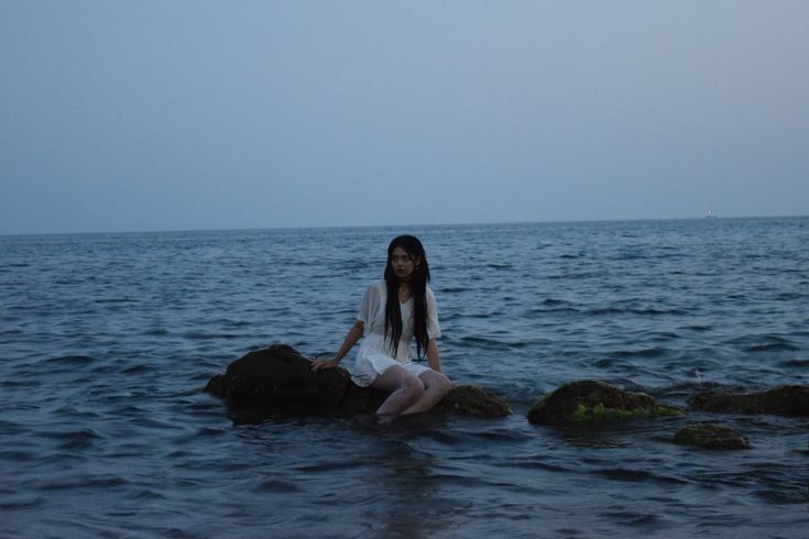 a woman sitting on top of a rock in the middle of the ocean at night