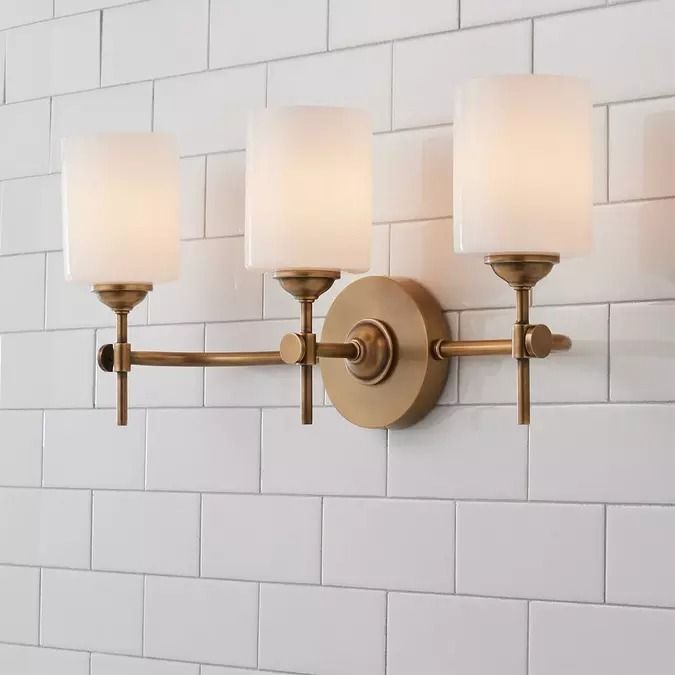 a bathroom light that is on the wall with three lights in front of white tiles