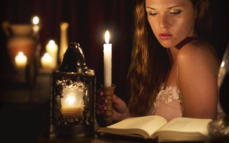 a woman sitting at a table with an open book and lit candle in front of her