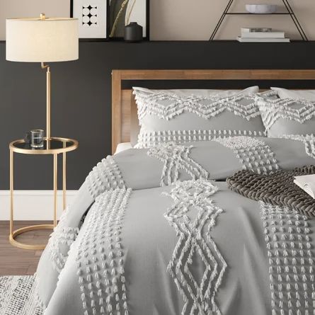 a bed with grey and white comforters in a room next to a lamp on a table