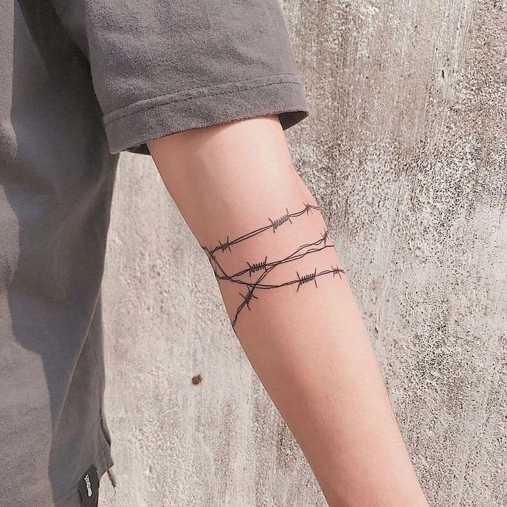 a person with a barbed wire tattoo on their arm and wrist is standing in front of a concrete wall