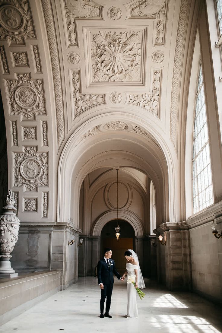 a bride and groom are standing in an ornate building with large windows on the ceiling