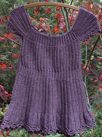 a purple knitted sweater hanging on a clothes rack in front of some trees and flowers