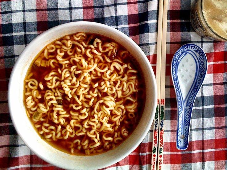 a bowl of ramen and chopsticks on a checkered table cloth next to a spoon