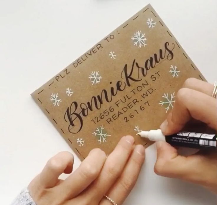 someone is writing on a brown card with white snowflakes